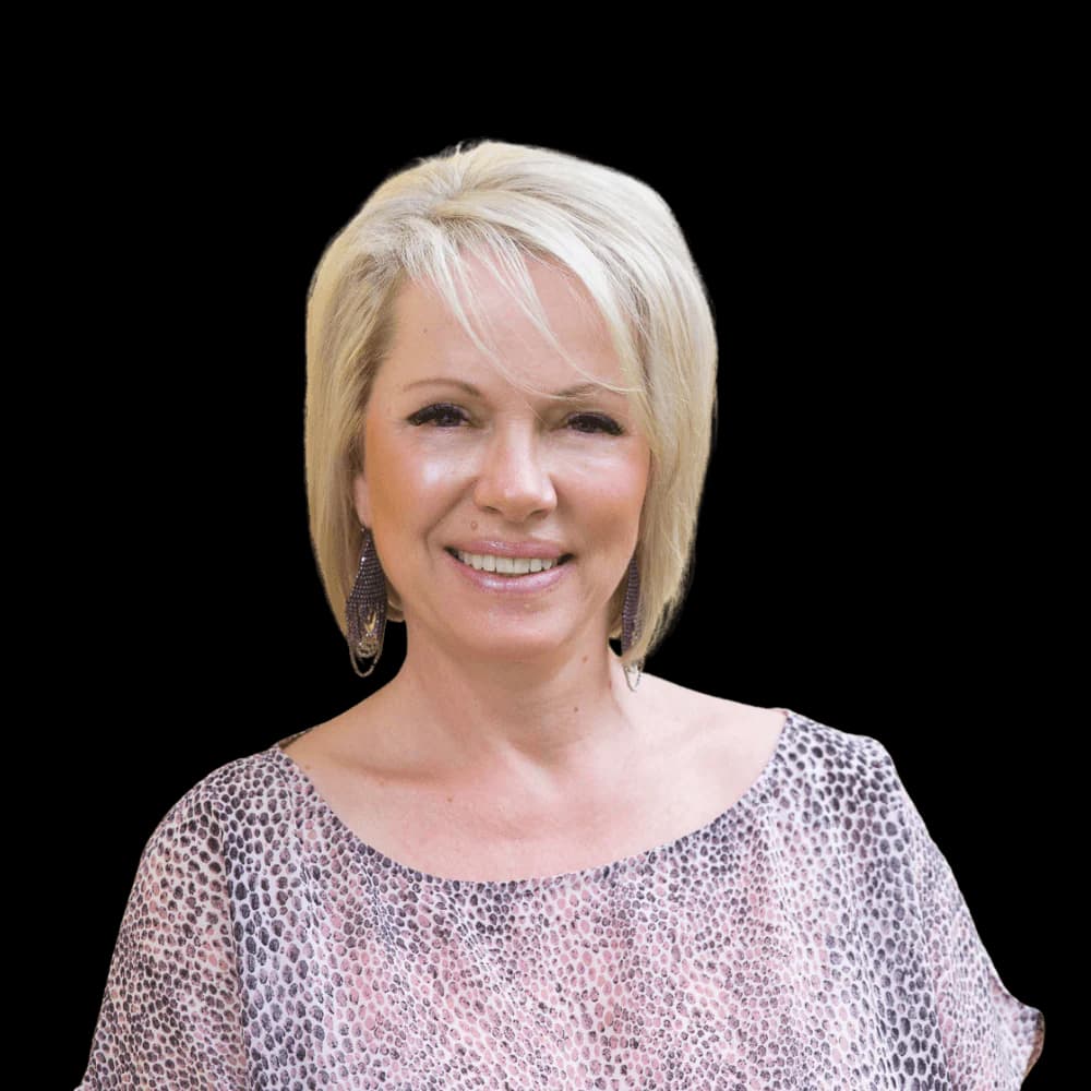 Smiling woman with short blonde hair wearing a pink animal print top on black background.